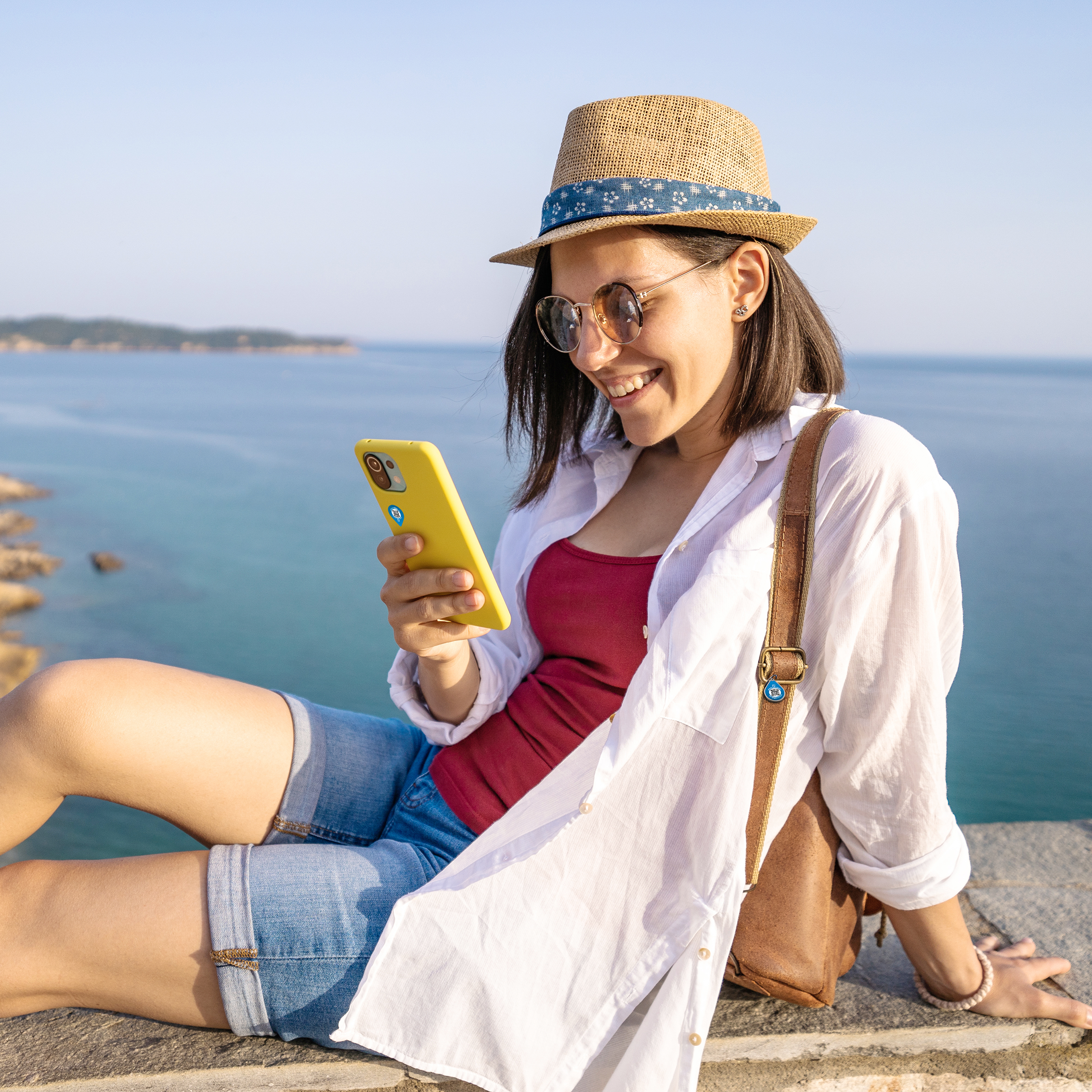 Eine Frau im Urlaub, sieht auf ihr Smartphone und freut sich, dass ihre Rucksack zurück kommt.